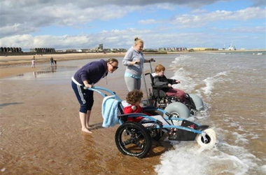 Children in beach wheelchairs being helped into sea