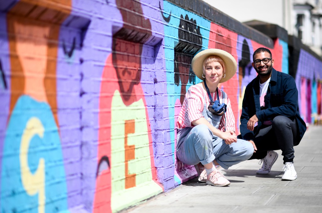 A man and a woman looking proud next to a colourful mural they have created